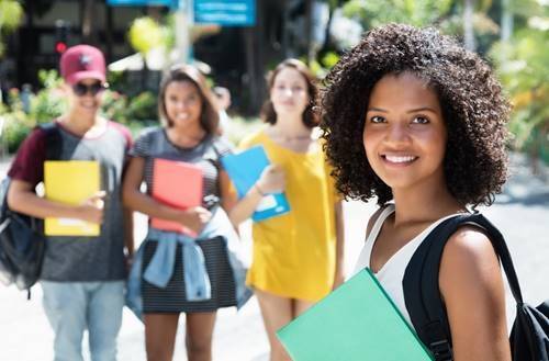 Young woman smiling and holding a book with her peers behind her. 