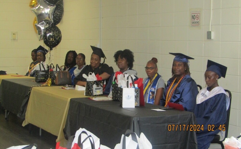 A line of graduates sitting behind some tables.