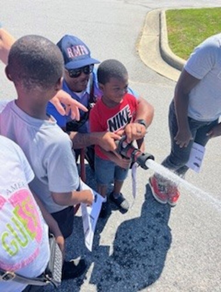 A little boy holding a water hose with help from a member of the Rocky Mount Fire Department.